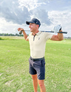Golfer wearing cream Forgiveness Polo and holding a club behind his shoulders on the fairway