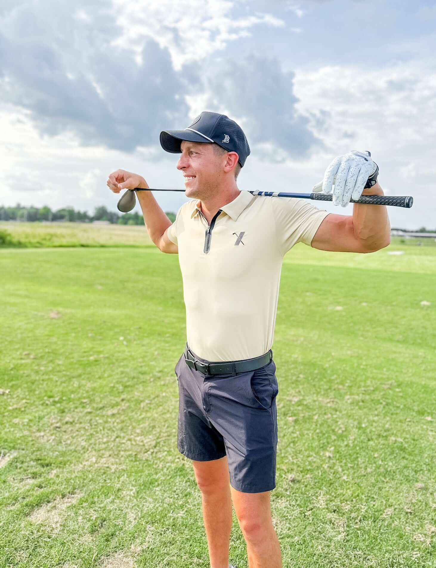 Golfer wearing cream Forgiveness Polo and holding a club behind his shoulders on the fairway